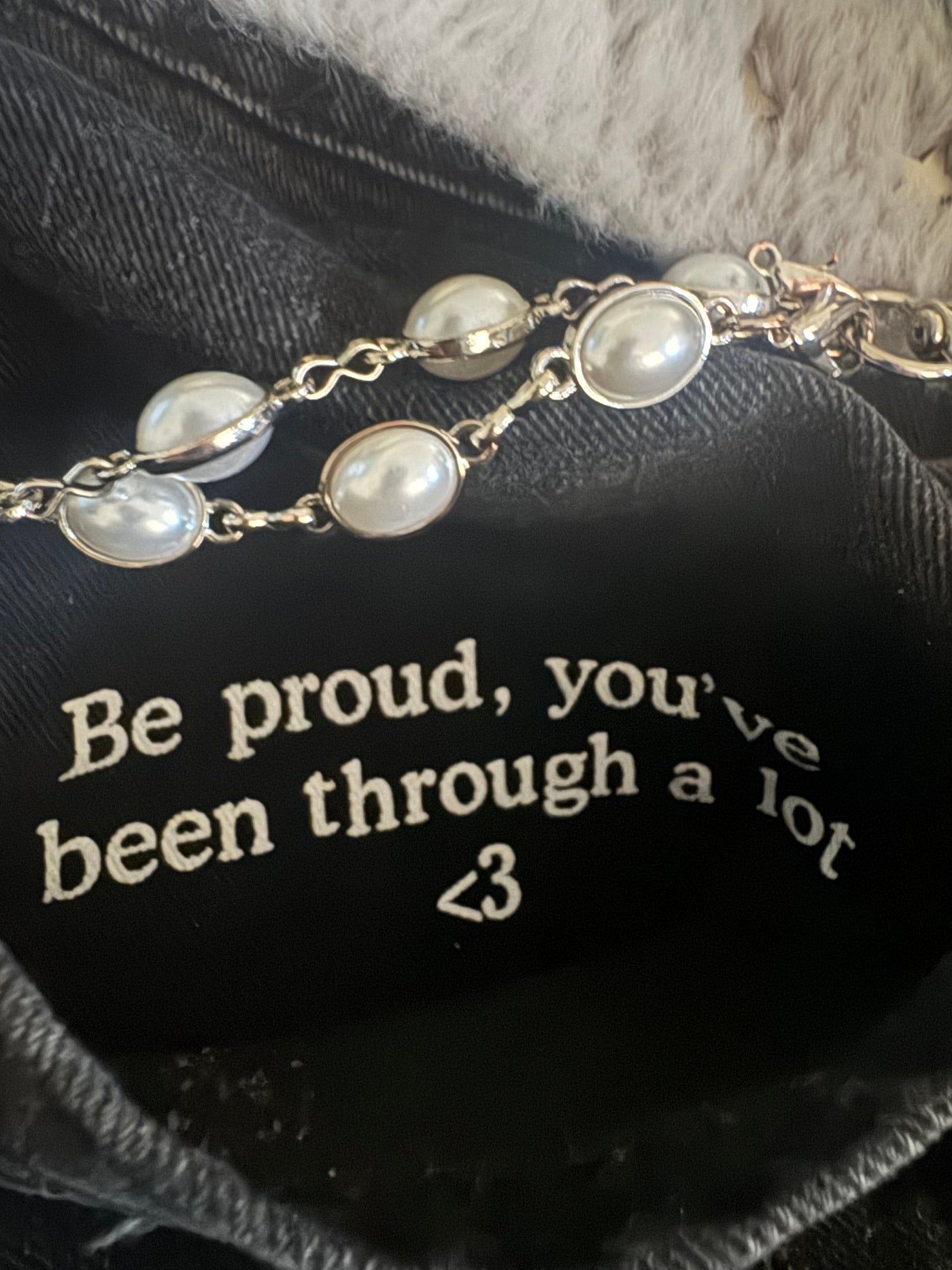 Inspirational message inside Resurge Jeans pocket reads 'Be proud, you’ve been through a lot <3' next to a pearl bracelet.